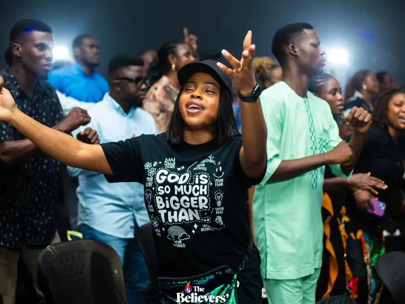 A young woman worshipping with hands raised amid the congregation.